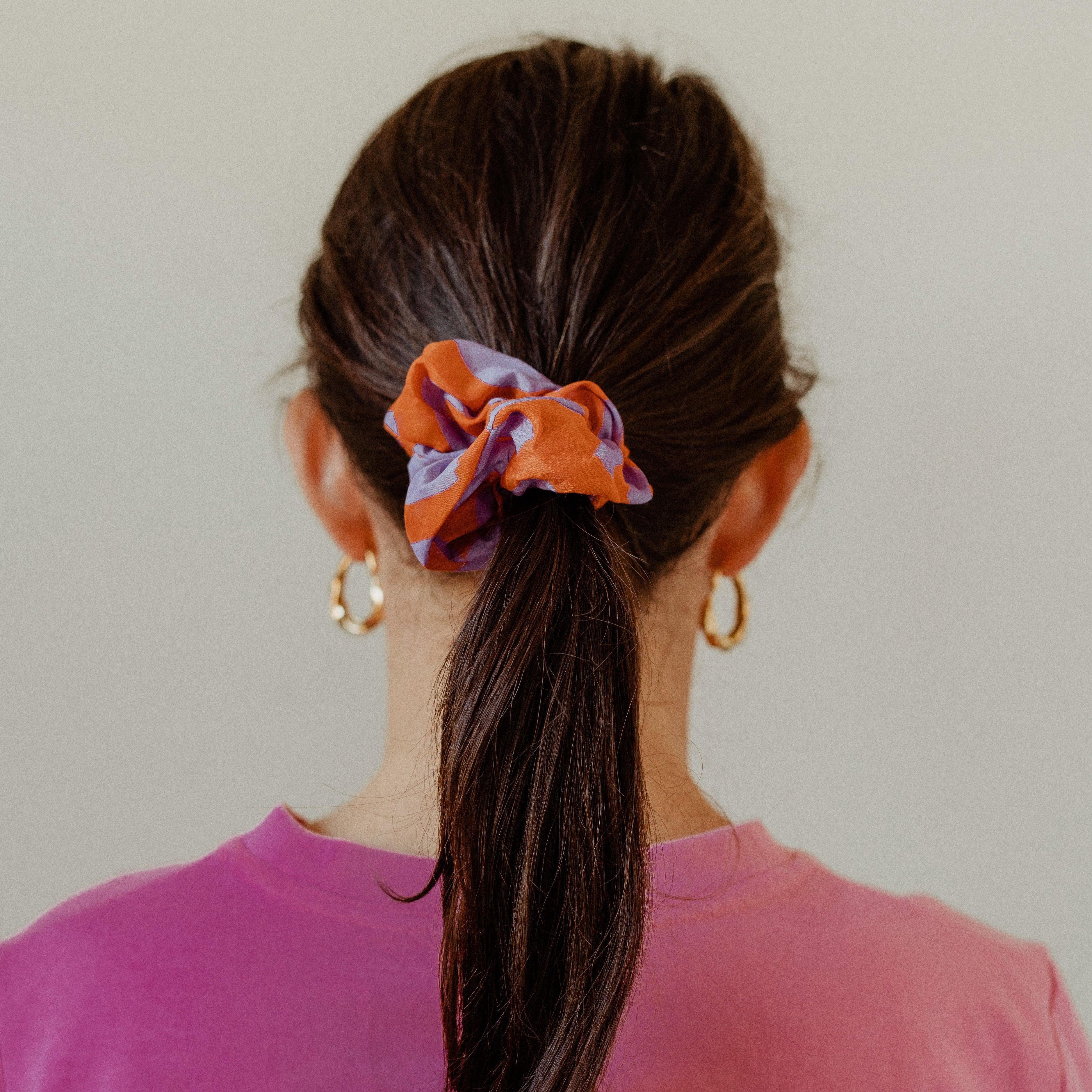 Person with a ponytail wearing an orange scrunchie against a plain background