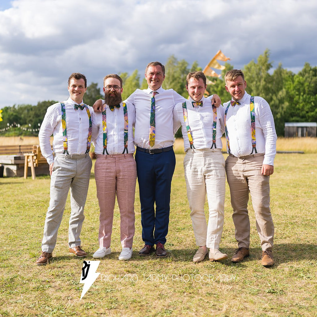 Five men standing together in a field with a cloudy sky and trees in the background.