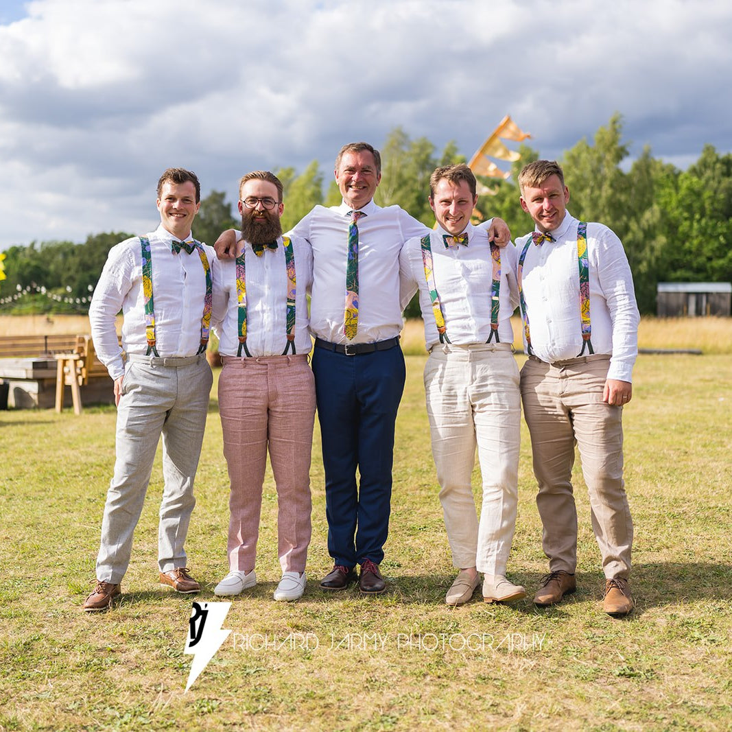 Five men standing together in a field with a cloudy sky and trees in the background.
