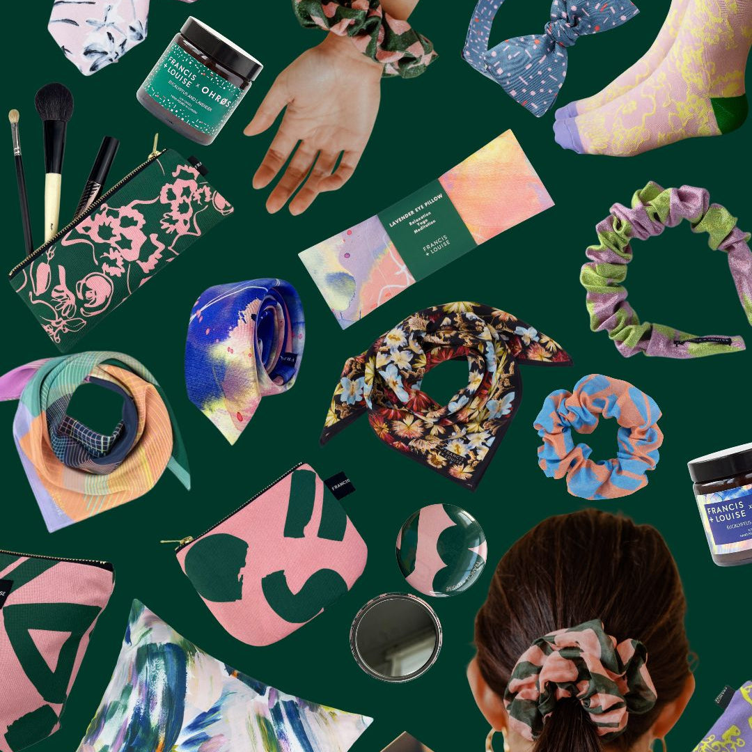 A flat-lay collage of fashion accessories and beauty items on a dark green background, including patterned scrunchies worn on a hand and head, a pink pouch, a floral zip pouch, a notebook, a small mirror, and other coordinated accessories.