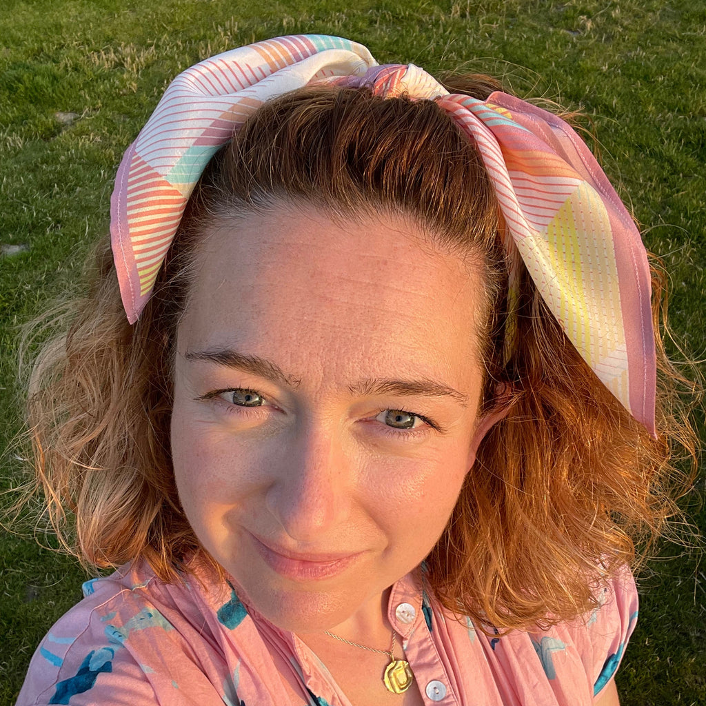 Person wearing a colorful headband and pink floral dress lying on grass
